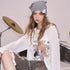 Person sitting on a drum set wearing a white oversized shirt with graphics and camouflage pants, with 'ELF SACK' branding.
